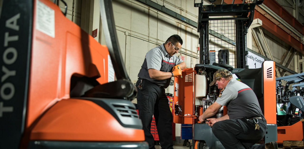 Two Toyota technicians beside a forklift with an open service panel