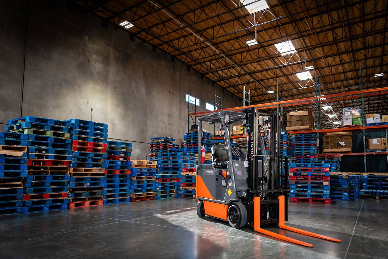 Toyota electric forklift parked among stacked pallets and warehouse racking