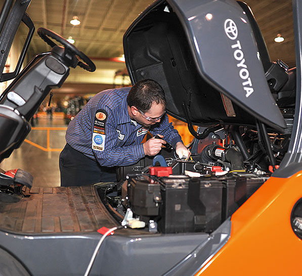Toyota technician working beside an open forklift service compartment
