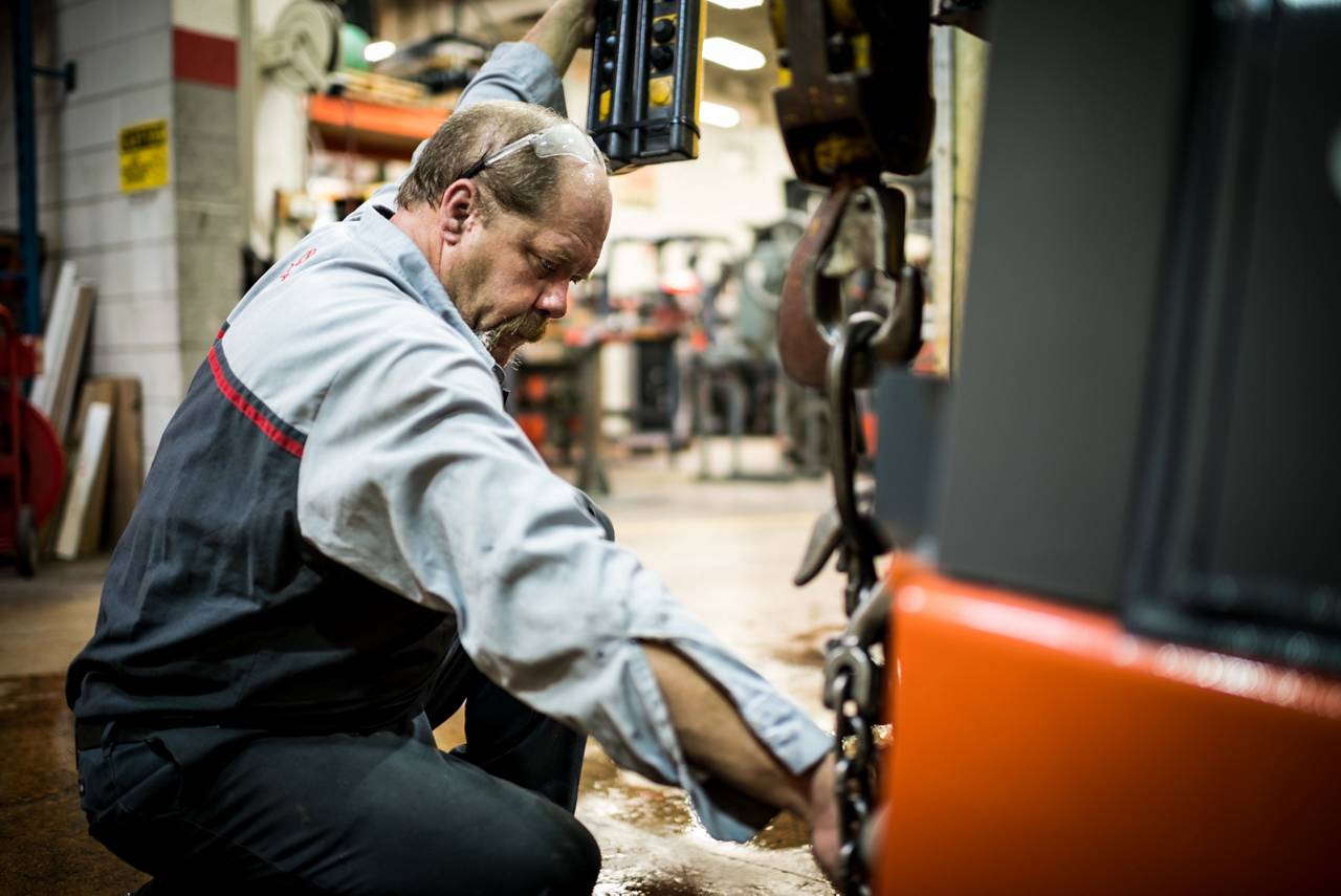 Toyota technician kneeling beside a forklift during equipment service