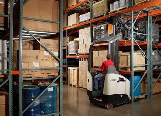 Operator using a Crown reach truck between warehouse pallet racks