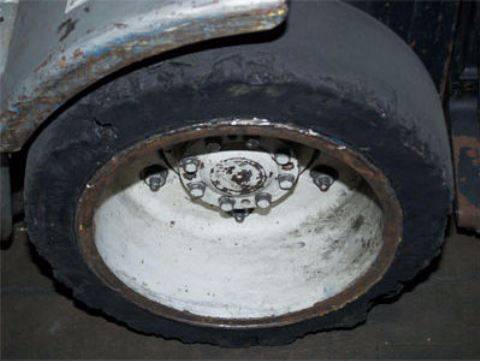 Damaged forklift tire with missing and uneven rubber around its edge